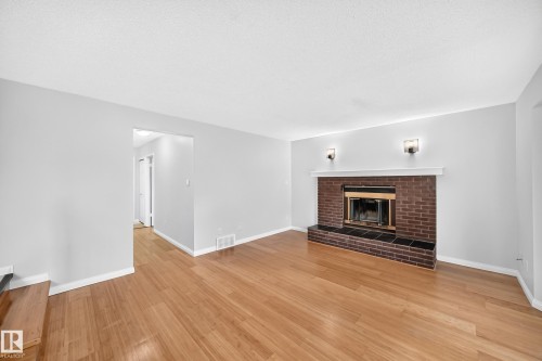 Spacious interior room featuring wood-finish flooring and a brick fireplace with a white mantel and two wall sconces - 9843 188 Street, Edmonton, AB 