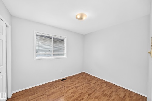 Room featuring wood-finish flooring, white baseboards, a flush-mount ceiling light, and a white-framed window with horizontal blinds - 9843 188 Street, Edmonton, AB 