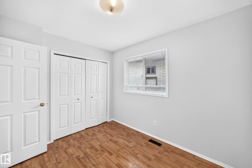 Room featuring wood-finish flooring, a double bi-fold closet, and a window with blinds - 9843 188 Street, Edmonton, AB 