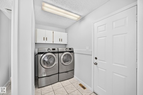 Laundry area featuring tile flooring, white wall cabinetry with bronze hardware, and a paneled entry door - 9843 188 Street, Edmonton, AB 