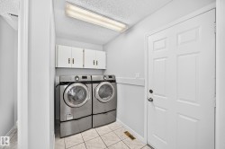 Laundry area featuring tile flooring, white wall cabinetry with bronze hardware, and a paneled entry door - 