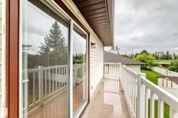 Outdoor balcony featuring white vinyl railings, a light-colored non-slip surface, and a sliding glass door with a brown frame - 