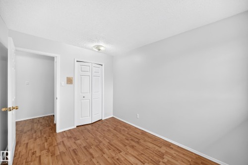 Interior room with light gray walls, wood-finish flooring, white bi-fold closet doors, and a ceiling-mounted light fixture - 9843 188 Street, Edmonton, AB 