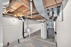 Utility area featuring exposed wood ceiling joists, white wall panels, a utility sink, a water heater, and a furnace unit - 