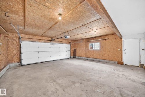 Spacious garage featuring a concrete floor, plywood walls, and a white paneled garage door - 9843 188 Street, Edmonton, AB 