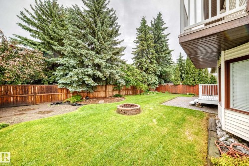 Spacious backyard featuring a lush lawn, a built-in stone fire pit, a paved patio, and a white deck with railings - 9843 188 Street, Edmonton, AB 