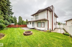 Expansive backyard featuring a brick fire pit, a paved patio area, and a white vinyl-sided exterior - 