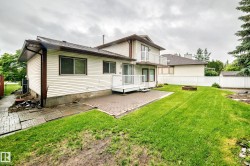 Expansive backyard featuring a lush lawn, paver patio, second-story balcony with white railing, and a ground-level deck with white railing - 