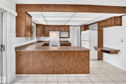Spacious kitchen featuring extensive wood cabinetry, white tile flooring, a U-shaped countertop configuration, a built-in breakfast bar, and white appliances - 