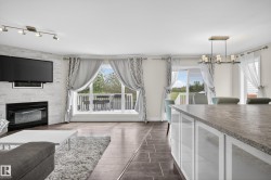 Combined living and dining space featuring a white brick fireplace, wood-finish flooring, and a large sliding glass door opening to an outdoor deck - 