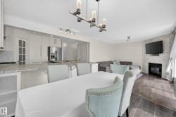 Open-concept living space featuring a dining area with contemporary chandelier, kitchen island with stone countertop, stainless steel refrigerator, and a living area with a fireplace - 