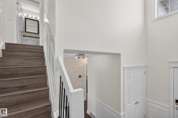 Two-story foyer with wood-finish flooring on stairs, white wainscoting, and a white window with grids - 