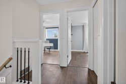 Upper hallway featuring dark wood-finish flooring, white trim, and a staircase with black metal balusters and a wood handrail - 