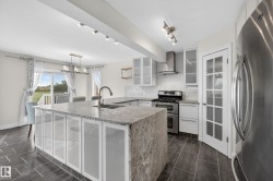 Kitchen featuring a stone-clad island with integrated sink, white cabinetry with frosted glass panels, stainless steel appliances, and dark tile flooring - 