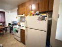 Kitchen area featuring wood-finish upper cabinetry, white appliances, and vinyl flooring - 38 11265 31 Avenue, Edmonton, AB 