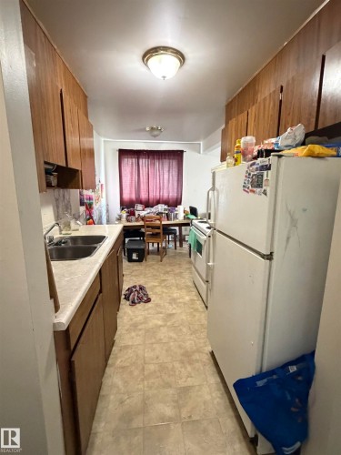 Galley kitchen featuring wood-finish cabinetry, a dual basin stainless steel sink, and light-toned countertop - 38 11265 31 Avenue, Edmonton, AB 