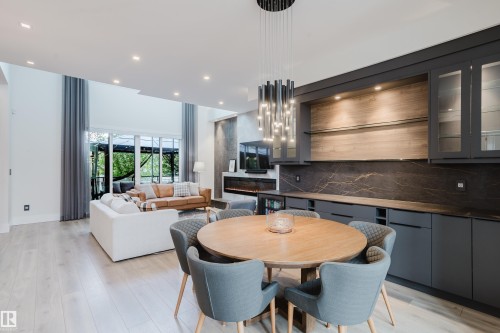 Open-concept living space featuring wood-finish flooring, a contemporary built-in bar with dark cabinetry and a patterned stone backsplash, and a modern linear fireplace - 1313 Clement Crest, Edmonton, AB 