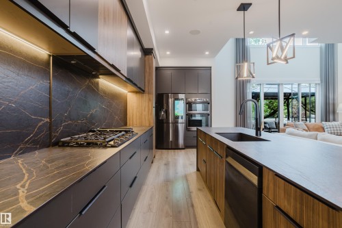 Gourmet kitchen with dark cabinetry, light wood-finish flooring, and a large central island - 1313 Clement Crest, Edmonton, AB 
