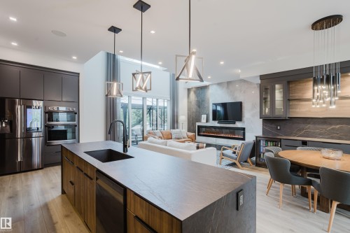 Spacious kitchen island with an integrated sink and matte black faucet, surrounded by contemporary cabinetry and stainless steel appliances - 1313 Clement Crest, Edmonton, AB 