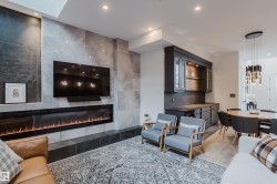 Living area featuring a floor-to-ceiling tiled fireplace surround, an elongated electric fireplace, a wall-mounted television, built-in cabinetry with glass doors, and recessed lighting - 