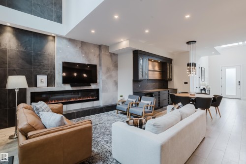 Spacious interior featuring a full-height tiled fireplace wall, an electric fireplace, built-in cabinetry with display shelving, recessed lighting, and light wood-finish flooring - 1313 Clement Crest, Edmonton, AB 
