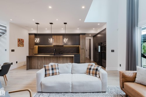 Modern kitchen featuring wood-finish and matte gray cabinetry, a waterfall island, black veined countertop and backsplash, and integrated appliances - 1313 Clement Crest, Edmonton, AB 