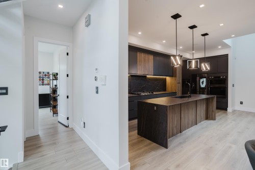 Modern kitchen featuring dark cabinetry, integrated appliances, and a central island with an undermount sink - 1313 Clement Crest, Edmonton, AB 