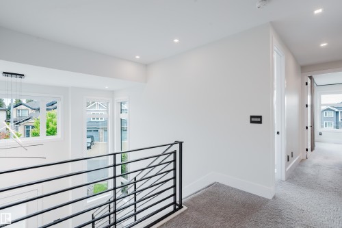 Contemporary interior hallway featuring recessed lighting, a modern chandelier, and a black metal railing - 1313 Clement Crest, Edmonton, AB 