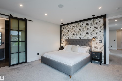 Carpeted bedroom featuring a patterned accent wall, recessed lighting, and a modern barn door with frosted glass panels - 1313 Clement Crest, Edmonton, AB 