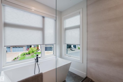 Freestanding soaking tub with a matte black floor-mounted faucet, set against two windows featuring roller shades - 1313 Clement Crest, Edmonton, AB 