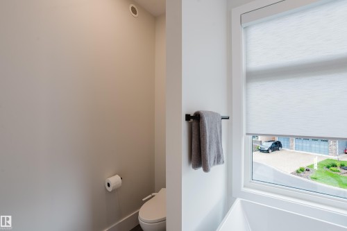 Modern bathroom featuring a window with a roller shade, a wall-mounted towel bar, and a toilet with an adjacent toilet paper holder - 1313 Clement Crest, Edmonton, AB 