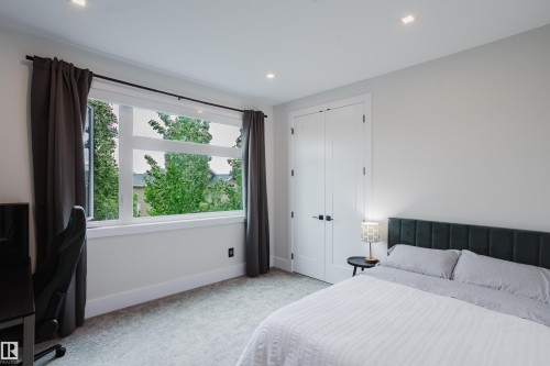 Bright room featuring a large window with white trim, recessed ceiling lighting, wall-to-wall carpeting, and a double-door closet with matte black hardware - 1313 Clement Crest, Edmonton, AB 
