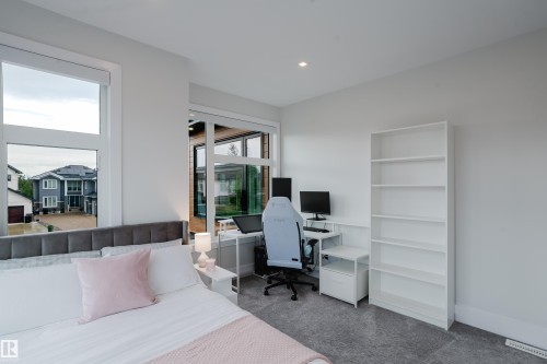 Carpeted room featuring a large bed with a fabric headboard, multiple windows, a recessed ceiling light, and a white built-in shelving unit - 1313 Clement Crest, Edmonton, AB 
