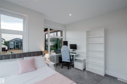 Carpeted room featuring a large bed with a fabric headboard, multiple windows, a recessed ceiling light, and a white built-in shelving unit - 
