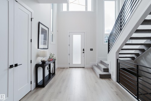 Two-story foyer featuring light wood-finish flooring and a contemporary staircase with black metal railings - 1313 Clement Crest, Edmonton, AB 