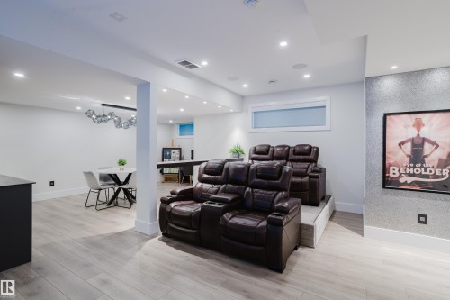 Entertainment area featuring tiered seating with two rows of upholstered recliners, wood-finish flooring, recessed lighting, and a horizontal transom window - 1313 Clement Crest, Edmonton, AB 