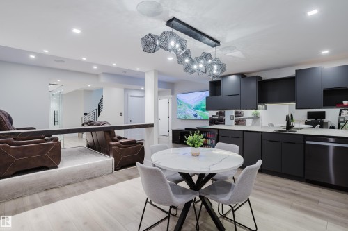 Modern lower level featuring a full kitchen with matte black cabinetry, light wood-finish flooring, recessed lighting, and a contemporary linear chandelier - 1313 Clement Crest, Edmonton, AB 