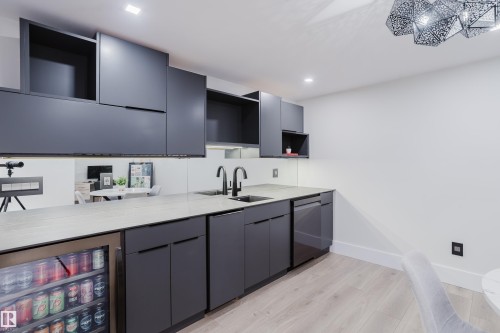 Wet bar featuring gray flat-panel cabinetry, light-toned countertops, two undermount sinks with matte black faucets, and an integrated beverage cooler - 1313 Clement Crest, Edmonton, AB 