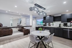 Modern lower level featuring a full kitchen with matte black cabinetry, light wood-finish flooring, recessed lighting, and a contemporary linear chandelier - 
