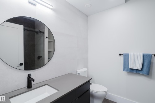 Modern bathroom featuring a rectangular integrated sink with a matte black faucet, dark vanity cabinetry, and a circular mirror - 1313 Clement Crest, Edmonton, AB 