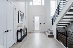 Two-story foyer featuring light wood-finish flooring and a contemporary staircase with black metal railings - 