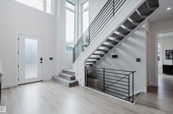 Grand entryway featuring a floating staircase with sleek horizontal iron railings, high ceilings, large windows, wood-finish flooring, and a frosted glass panel entry door - 