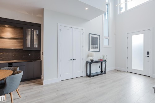 Light wood-finish flooring extending through an open living area featuring a custom built-in wet bar with dark cabinetry, integrated lighting, and a stone backsplash - 1313 Clement Crest, Edmonton, AB 
