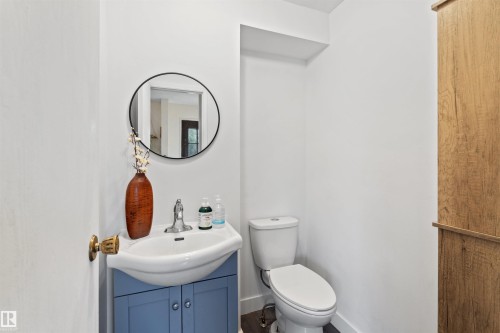 Powder room featuring a pedestal sink with a blue vanity, a round wall-mounted mirror, and a white toilet - 359 Kirkpatrick Crescent, Edmonton, AB 