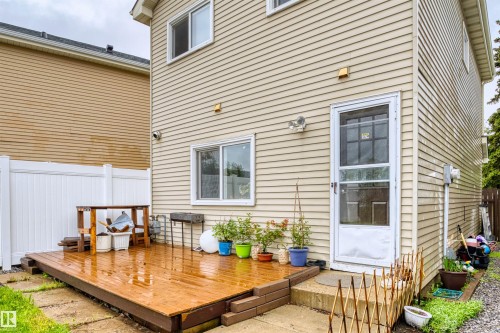 Rear exterior featuring beige horizontal siding, a ground-level wood-finish deck, white vinyl fencing, a white exterior door with a glass storm door, and a white-framed window - 359 Kirkpatrick Crescent, Edmonton, AB 