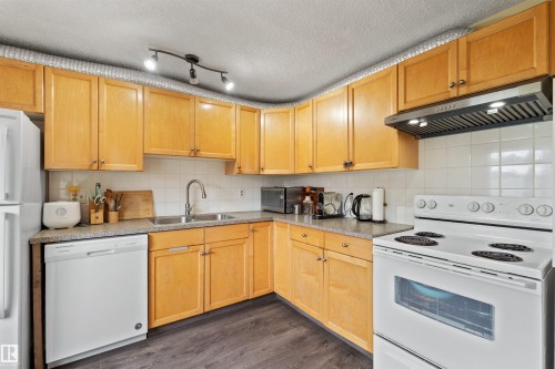 Kitchen featuring wood-finish cabinetry, white tile backsplash, a stainless steel sink with a gooseneck faucet, a built-in dishwasher, and wood-finish flooring - 359 Kirkpatrick Crescent, Edmonton, AB 