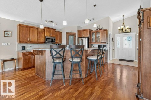 Open-concept kitchen featuring wood cabinetry, stainless steel appliances, a breakfast bar, and wood-finish flooring extending into the living area - 39 Wilkinson Place, Leduc, AB 