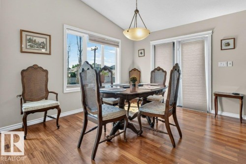Dining area featuring wood-finish flooring, vaulted ceiling, and ample natural light from the large window and sliding glass door - 39 Wilkinson Place, Leduc, AB 