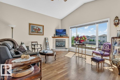 Living area featuring wood-finish flooring, a corner fireplace with a tile surround and mantel, a vaulted ceiling, and large picture windows - 39 Wilkinson Place, Leduc, AB 
