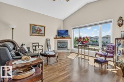 Living area featuring wood-finish flooring, a corner fireplace with a tile surround and mantel, a vaulted ceiling, and large picture windows - 